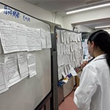 研究記録をホワイトボードに貼り眺める学生